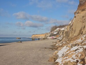 Eine Küstenlandschaft mit Sandstrand, Felsenküste und blauem Himmel.