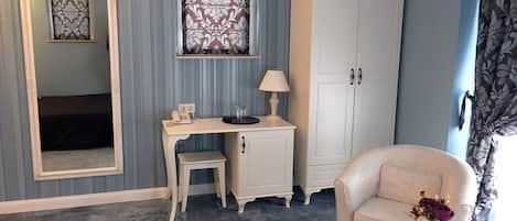 Une pièce comprenant un bureau, une chaise, une armoire, un miroir et une petite table sur laquelle est posé un vase.