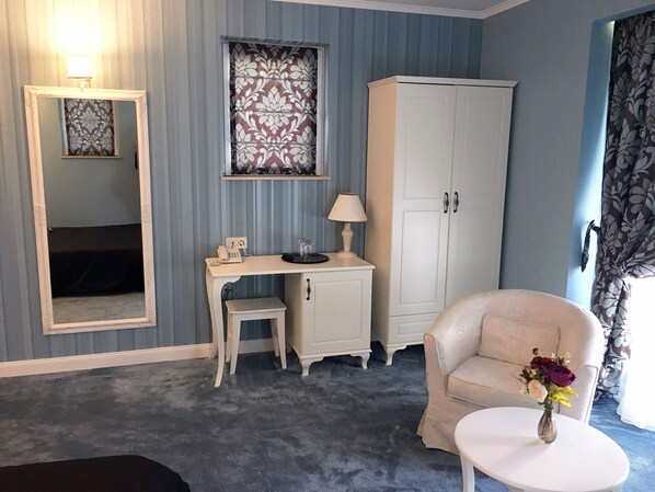 A room with a desk, a chair, a wardrobe, a mirror, and a small table with a vase.
