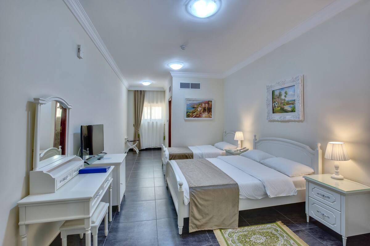 A hotel room with two beds, a desk, a mirror, a TV, and a painting on the wall.