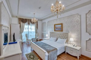 A hotel room with a large bed, a chandelier, a desk with a chair, and a television.