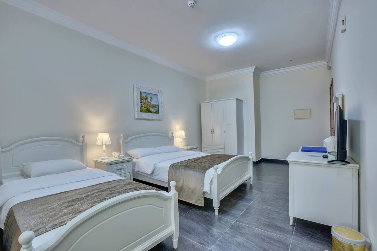 A hotel room with two beds, a desk, a wardrobe, and a painting on the wall.