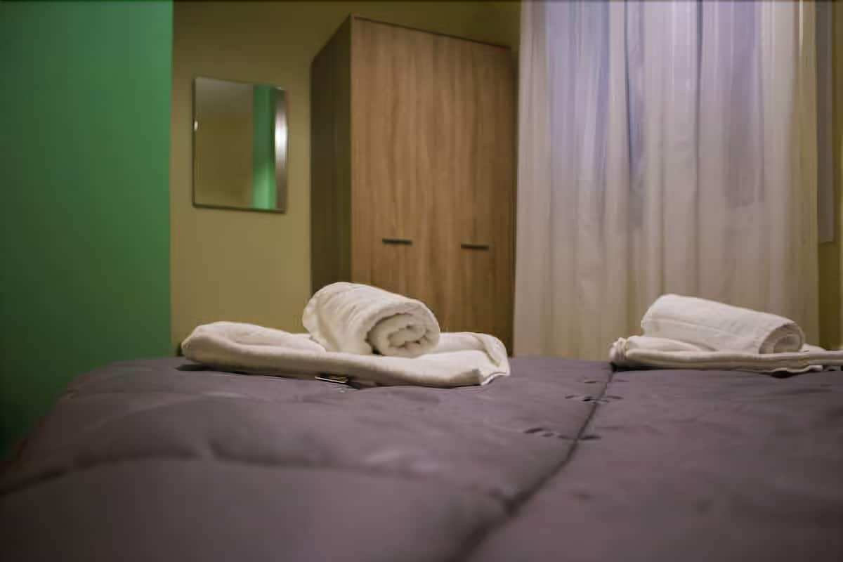 A bedroom with a bed, two rolled towels, a wooden wardrobe, and a mirror on the wall.