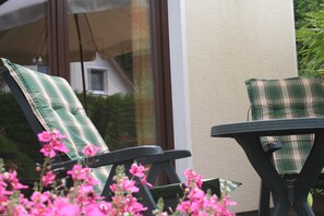 Two lounge chairs with plaid cushions, a small table, and pink flowers in the foreground. - Am Norderfeld, Ground Floor - Am Norderfeld, First Floor, Ground Floor (Wustrow)