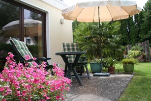 Une terrasse avec une table et des chaises, une plante en pot et un grand parasol.