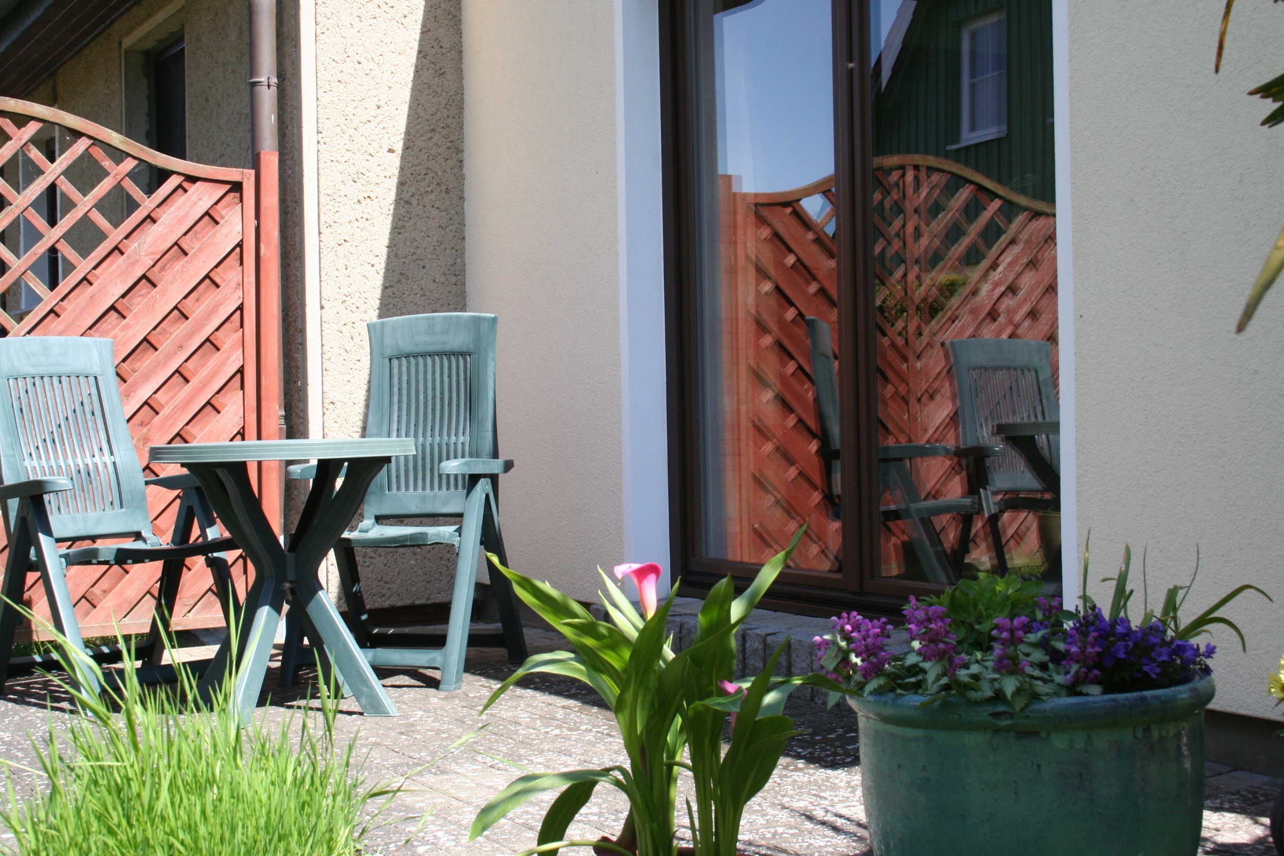 An outdoor seating area with a table and chairs, a wooden fence, and potted plants.