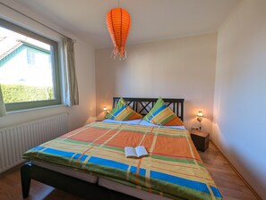 Een slaapkamer met een bed, een raam, een hanglamp en bedlampjes.