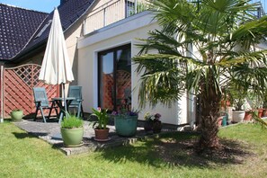 Een huis met een terras, tuinmeubilair en plantenpotten.