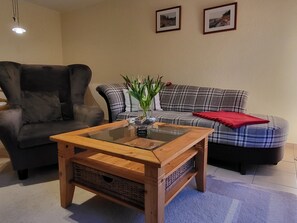 A living room with a dark armchair, a plaid sofa, a glass-top coffee table, and two framed pictures on the wall. - Am Norderfeld, Ground Floor - Am Norderfeld, First Floor, Ground Floor (Wustrow)