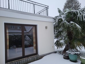 A modern building with a large glass door, a balcony with metal railings, and a snow-covered palm tree. - Am Norderfeld, Ground Floor - Am Norderfeld, First Floor, Ground Floor (Wustrow)