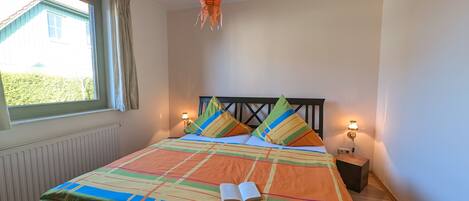 A bedroom with a bed, a window, a hanging light fixture, and bedside lamps.
