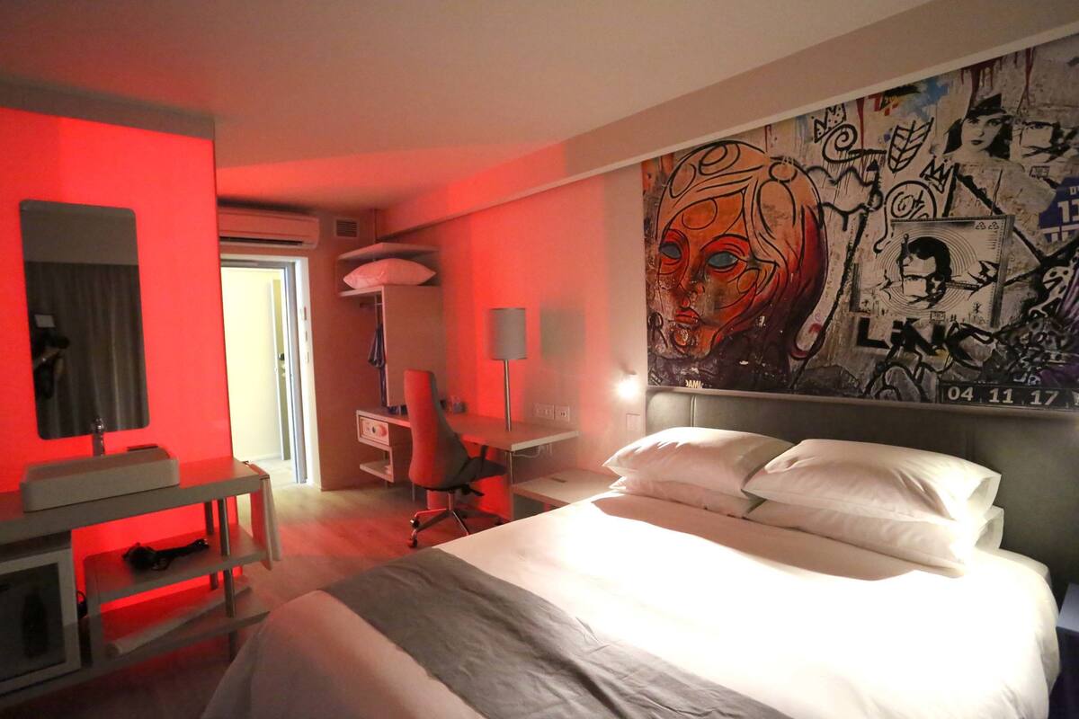 Ein Hotelzimmer mit Bett, Schreibtisch, Stuhl und einer Wand mit Graffiti-Kunst.