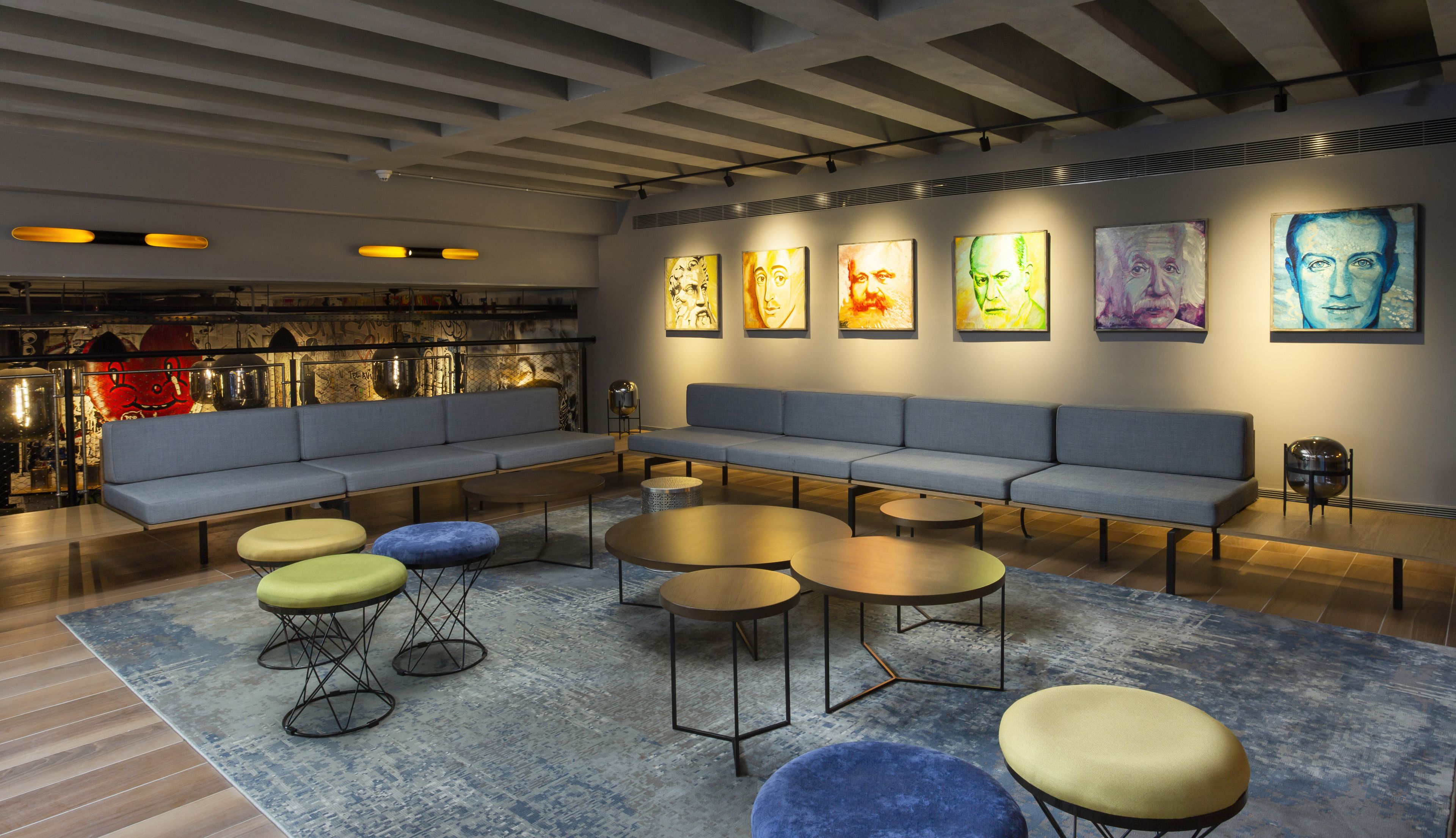 A modern lounge area with a grey sofa, round coffee tables, and colorful ottomans.