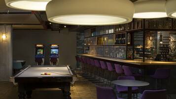 A billiards table, bar area with purple chairs, and arcade machines.