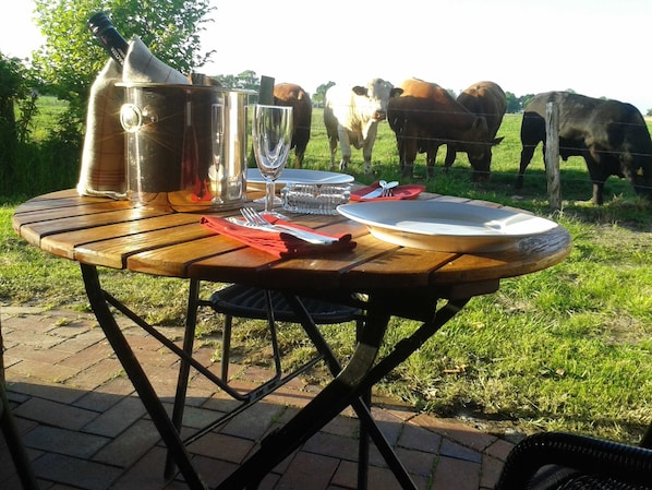 A wooden table set outdoors with a bottle, glasses, and plates.