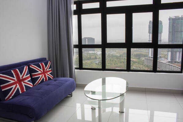 A room with a blue sofa, two pillows with Union Jack designs, a glass table, and a large window offering a city view.