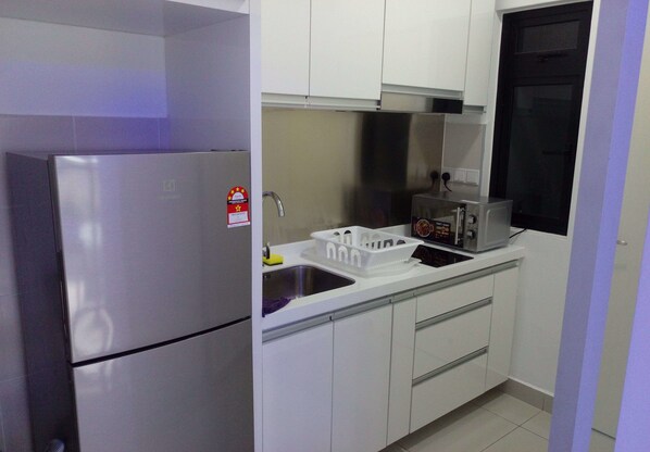 Una cocina compacta con gabinetes blancos, un refrigerador de acero inoxidable, un microondas y un lavamanos.