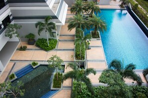Un área de piscina en la azotea con una vista despejada del cielo, rodeada de palmeras y una estructura de edificio moderna.