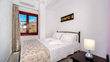 Una cama bien hecha con cubrecama acolchado, una lámpara de noche y una ventana con cortinas.