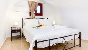 Una cama bien tendida con ropa blanca, una mesita de noche con una lámpara y una ventana con cortinas.