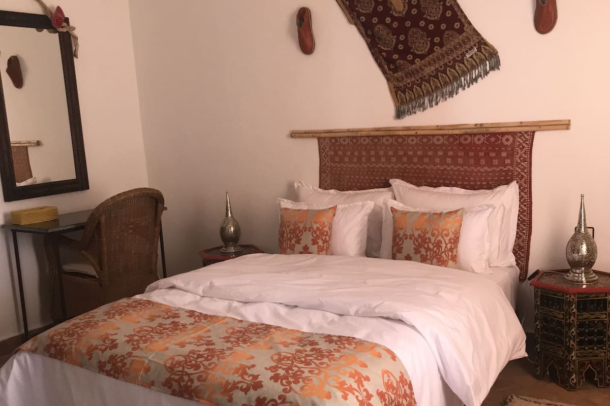 Ein ordentlich eingerichtetes Schlafzimmer mit Bett, Stuhl, kleinem Tisch und Wand-Klimaanlage.