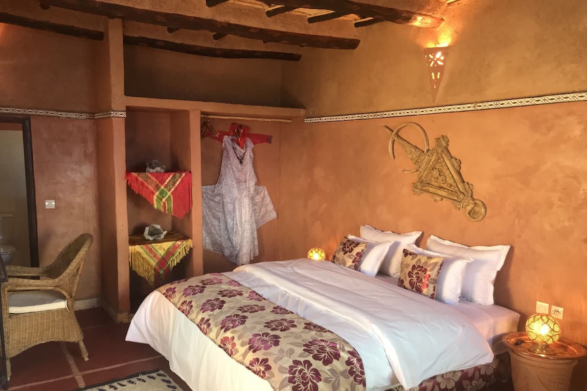 Ein Schlafzimmer mit einem Bett, einem Sessel, einer Kleiderstange und einer Wandleuchte.