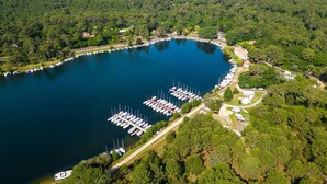 An aerial view of a marina surrounded by dense forest, with boats docked and a road leading to the area. - Charming Villa with Private Heated Pool, Near Golf, Lake, Beach, Surf, and Aqua Park (Biscarrosse)