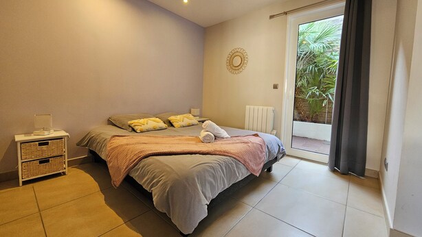 A bedroom with a bed, a nightstand, a radiator, and a view of greenery through the window.