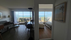 A room with a large window, a dining table, a sofa, and a bed.
