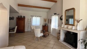 A spacious living room with a high ceiling, wooden beams, a fireplace, a sofa, and a dining area. - Near Avignon, Comfortable villa with private pool, in Provence  (Althen-Des-Paluds)