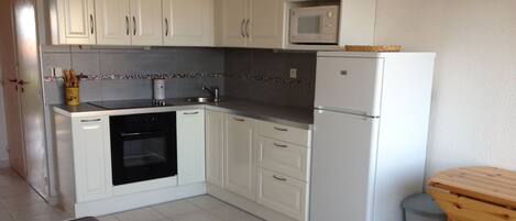 A compact kitchen with white cabinets, a built-in microwave, a refrigerator, and a small dining table.