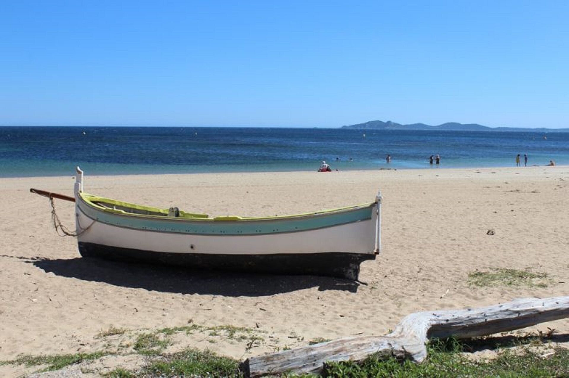 A boat on a sandy beach with a clear view of the ocean and distant mountains.