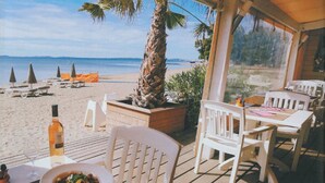 Un restaurant situé en bord de mer, avec une terrasse, une plateforme en bois et une vue sur la plage et l’océan.