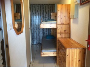 Une petite chambre comprenant un lit superposé, un petit bureau et un miroir.