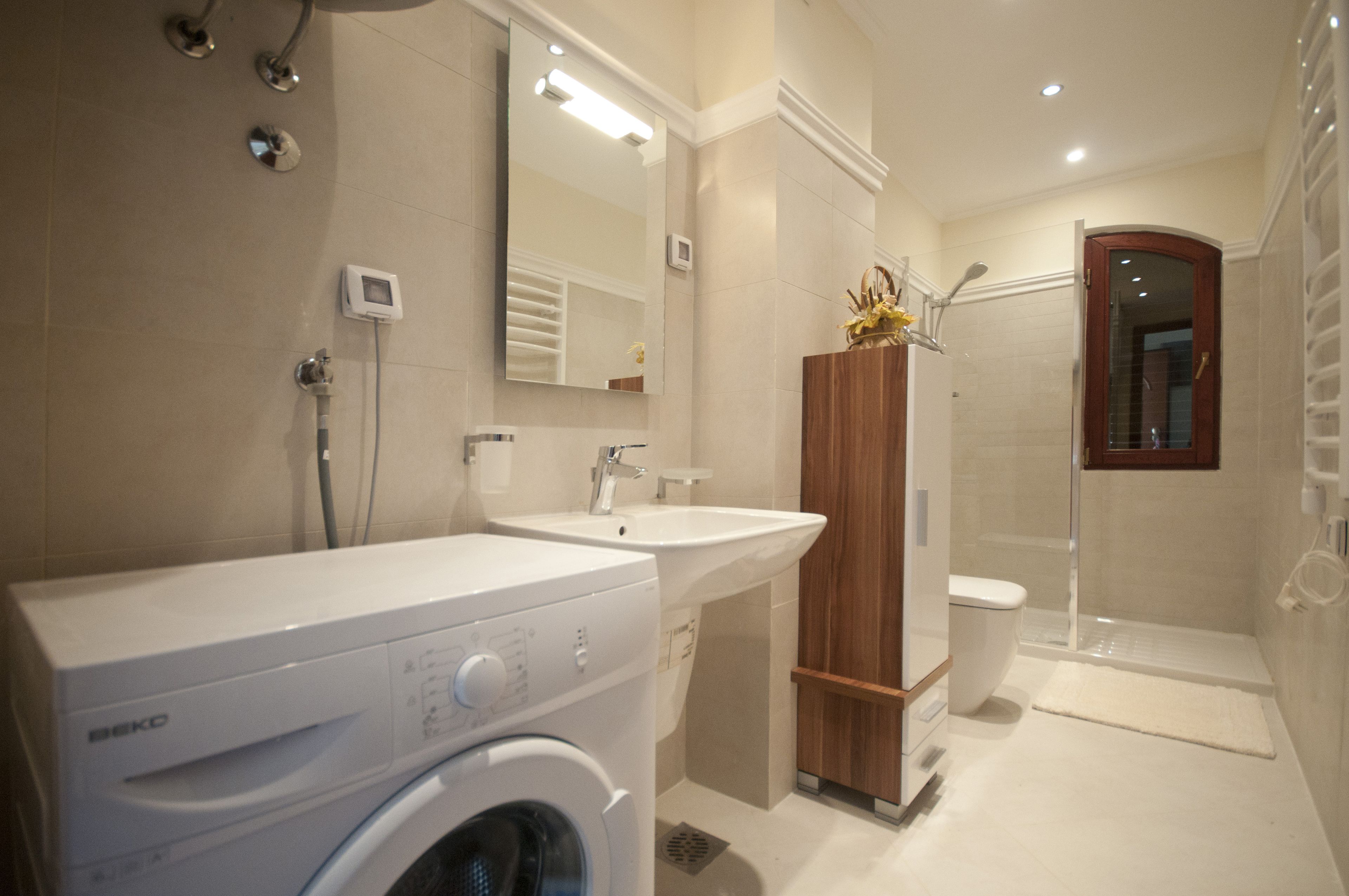 A modern bathroom with a washing machine, two sinks, a toilet, and a shower area.