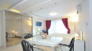 A modern hotel room with a glass dining table, two chairs, a bed with red curtains, a bedside lamp, and a TV on the wall. - St. George Apartments and Villa with pool (Petrovac)