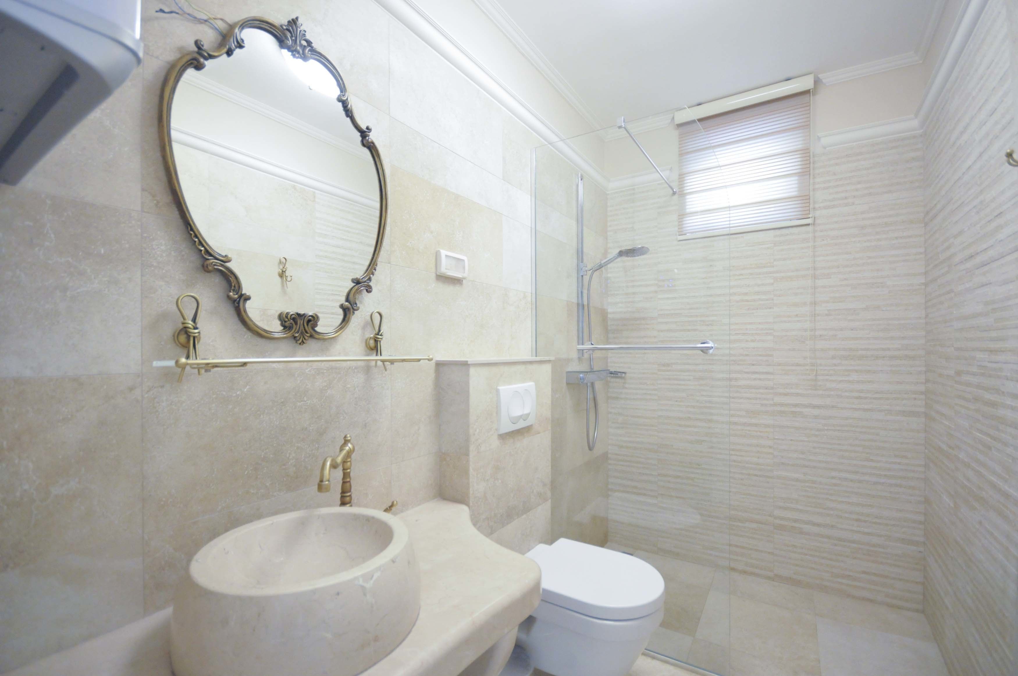 A bathroom with a large oval mirror, a sink, a toilet, and a glass-enclosed shower area.