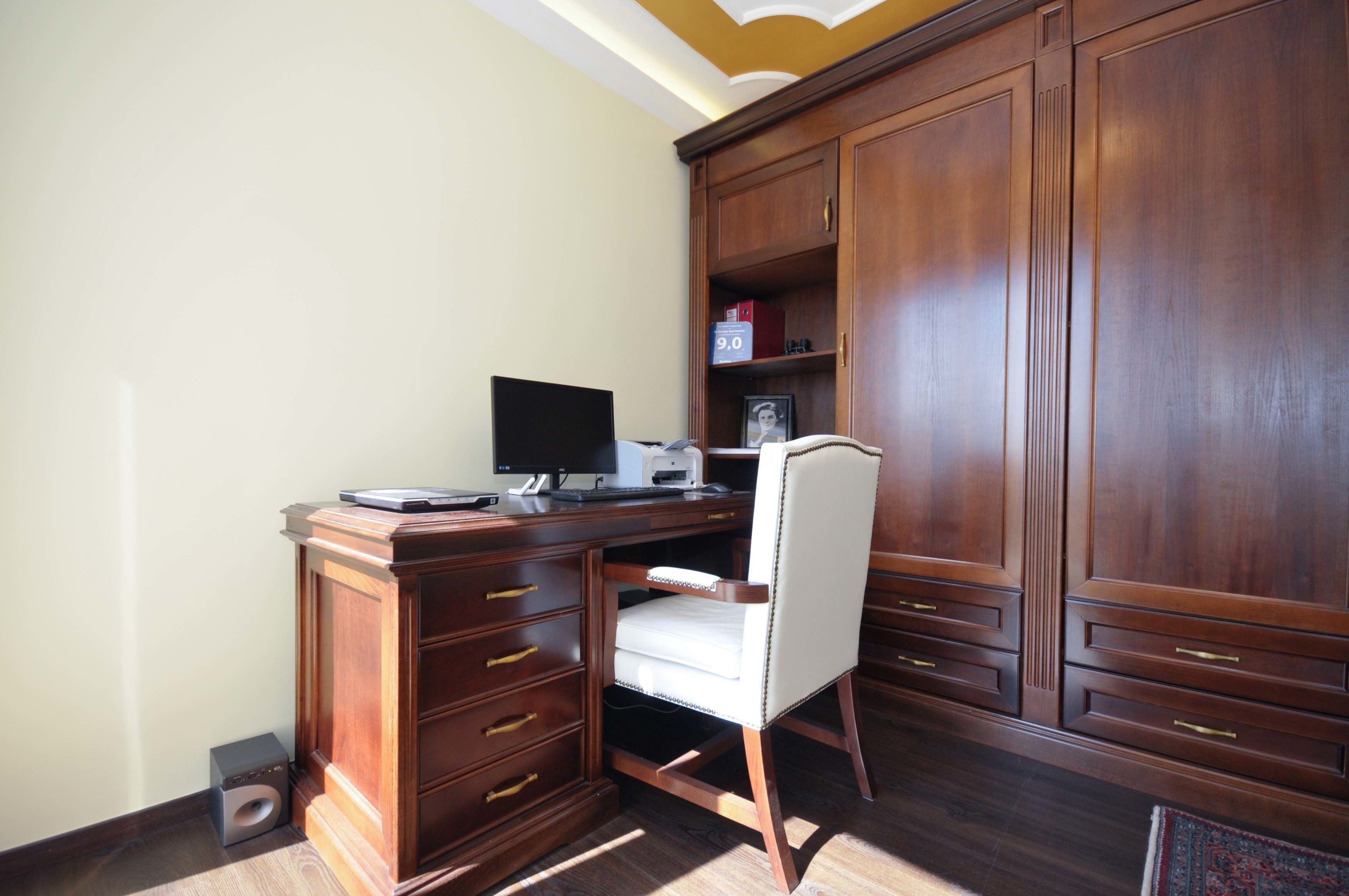 A wooden desk with a computer, a chair, and a cabinet with drawers.