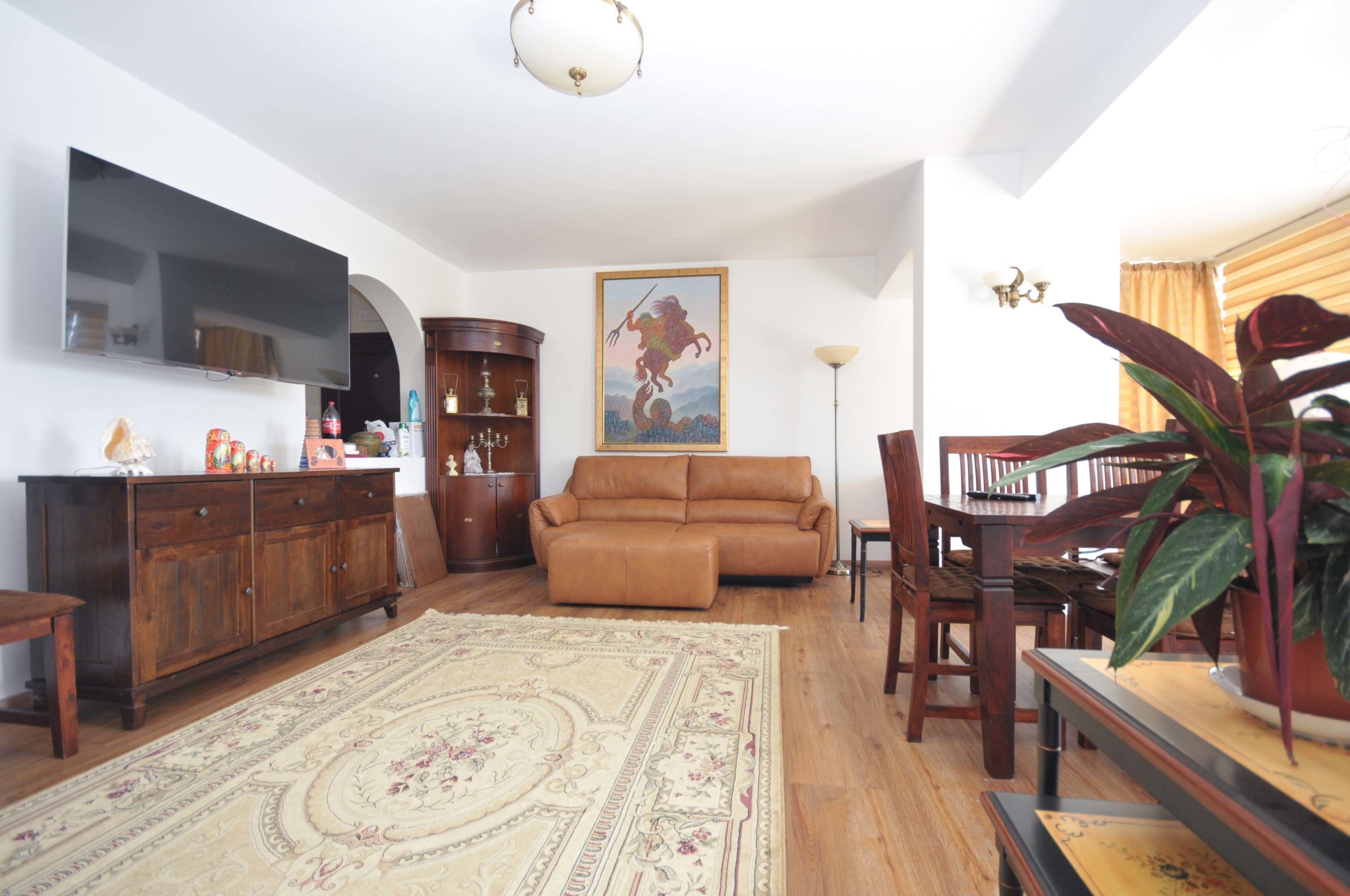 A living room with a brown sofa, wooden furniture, a flat-screen TV, a large rug, and a painting of a horse.