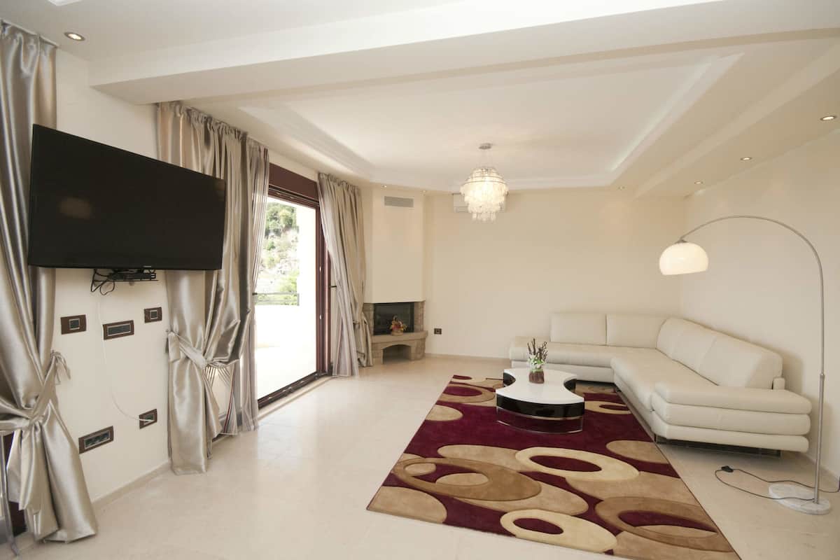A modern living room with a flat-screen TV, a white sofa, a round coffee table, and a patterned rug.