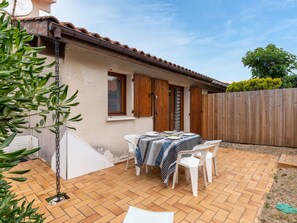 Une terrasse avec une table dressée pour le repas, une plante suspendue et une clôture en bois en arrière-plan.