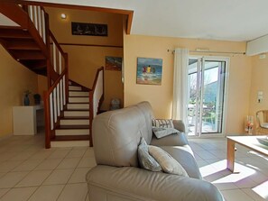 A living room with a beige sofa, a wooden staircase, and a painting of sailboats on the wall.