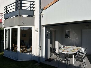Ein modernes Haus mit überdachter Terrasse, einem Esstisch für vier Personen und einem kleinen Balkon mit einem Stuhl.