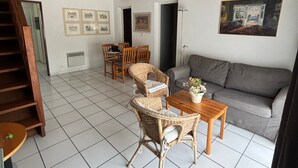 A spacious living area with a grey sofa, wicker chairs, a wooden table, and a staircase. - Beachside Duplex in a Quiet Area - Steps from Dunes & Shops - Parking & Cleaning Included (Biscarrosse Plage)