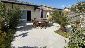 A patio with a table and chairs, surrounded by potted plants and a building with a tiled roof. - Beachside Duplex in a Quiet Area - Steps from Dunes & Shops - Parking & Cleaning Included (Biscarrosse Plage)
