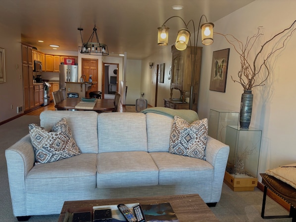 A living room with a sectional sofa, a coffee table, and a dining area with a wooden table and chairs.