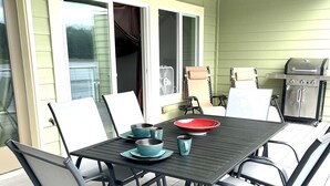 Une terrasse couverte avec une table dressée pour quatre personnes, entourée de chaises, et un barbecue à l’arrière-plan.