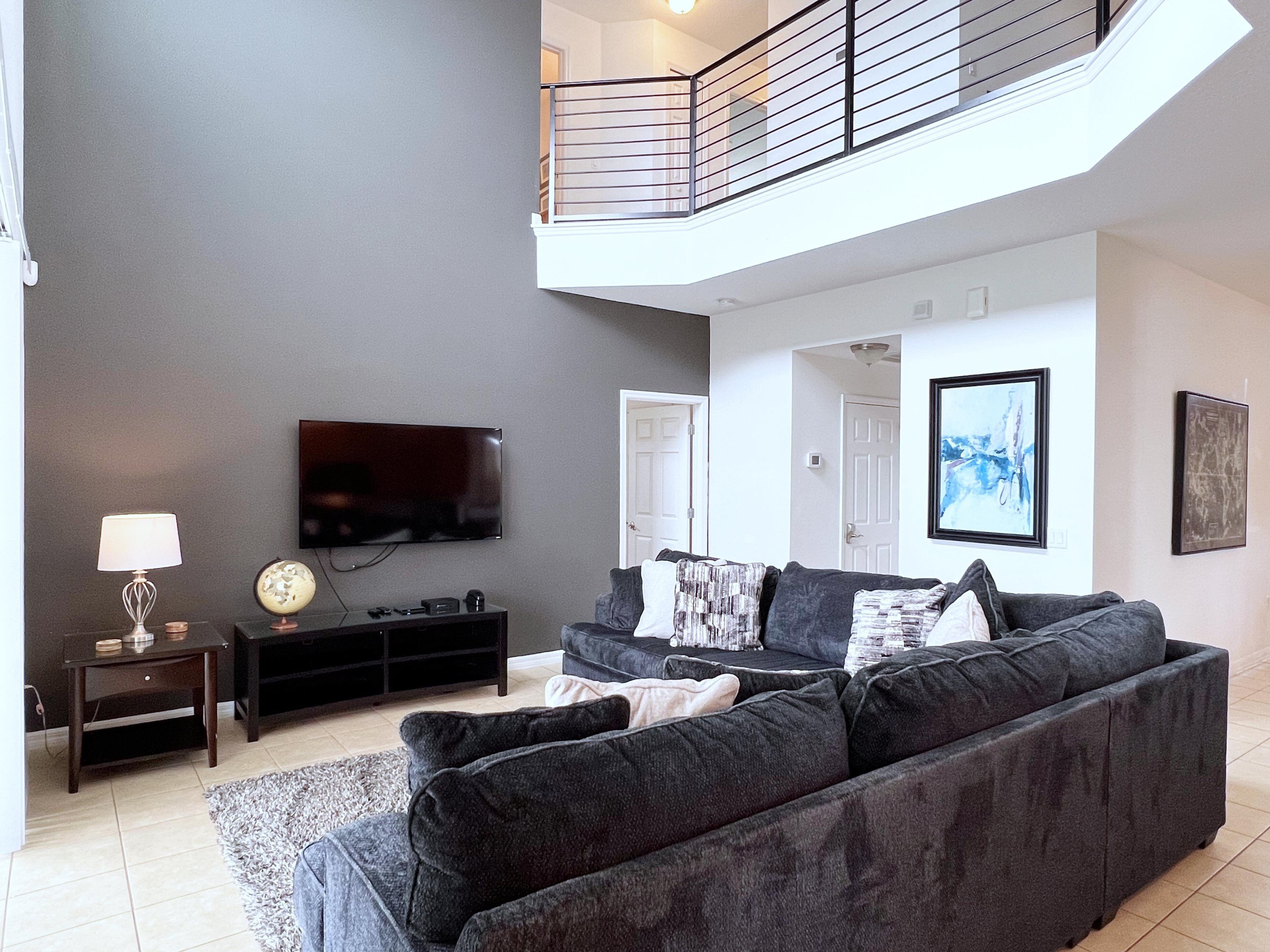 A modern living room with a grey sofa, a flat-screen TV, and a small table with a lamp.