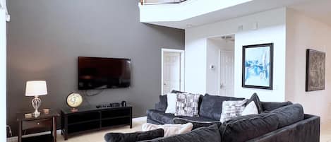A modern living room with a grey sofa, a flat-screen TV, and a small table with a lamp.