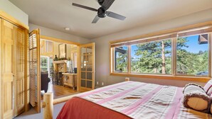 Un dormitorio con una cama grande, un ventilador de techo y una ventana con vistas a árboles.